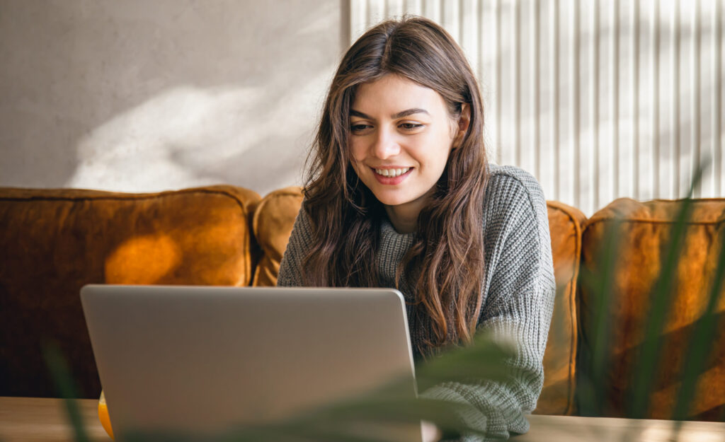 Attractive young woman working on a laptop early in the morning in an interior with sunlight.